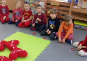 Grupka dzieci siedzi na dywanie ,przed nimi serduszka wygięte z drucika kreatywnego.
